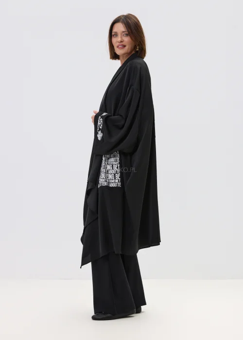 Czarne kimono damskie o luźnym, oversize’owym kroju z szerokimi rękawami i nadrukiem typograficznym, stylizacja w nowoczesnym, streetwearowym klimacie.