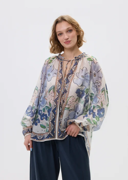 Zwiewna bluzka w odcieniach kremowo-niebieskich z kwiatowym wzorem i ozdobnym wiązaniem przy dekolcie, zestawiona z luźnymi spodniami w lekkiej, kobiecej stylizacji.