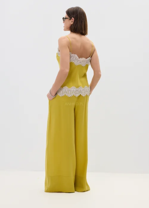 Żółty top damski na ramiączkach z koronkowym wykończeniem przy dekolcie i dole, lekki i elegancki, stylizowany z szerokimi spodniami w dopasowanym looku.