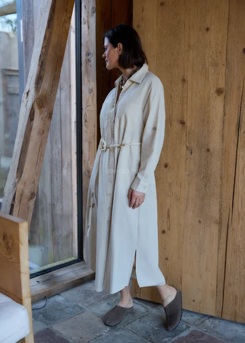 Beżowa sukienka koszulowa midi z dodatkiem lnu, z paskiem w talii, zapinana na guziki, z długim rękawem, minimalistyczna stylizacja casual.