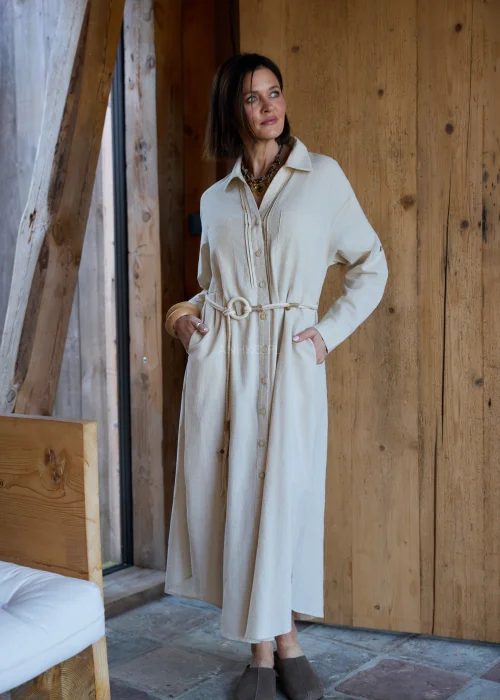 Beżowa sukienka koszulowa midi z dodatkiem lnu, z paskiem w talii, zapinana na guziki, z długim rękawem, minimalistyczna stylizacja casual.