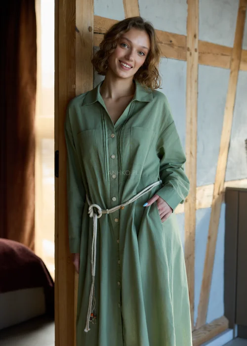 Zielona sukienka koszulowa midi z dodatkiem lnu, z paskiem w talii, zapinana na guziki, z długim rękawem, minimalistyczna stylizacja casual.