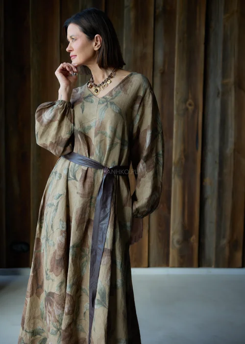 Brązowa sukienka lniana maxi w kwiatowy wzór z długim rękawem i paskiem w talii, luźny fason, styl naturalny i elegancki.
