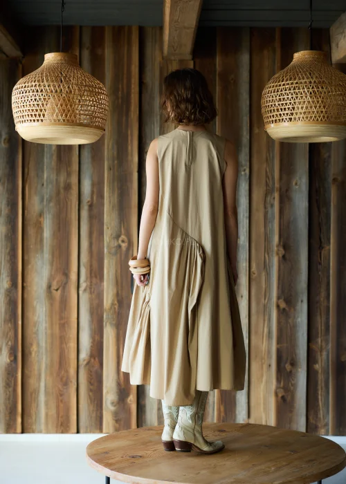 Camelowa sukienka midi o luźnym kroju bez rękawów, z asymetrycznym marszczeniem i rozcięciem, styl casual z kowbojkami.