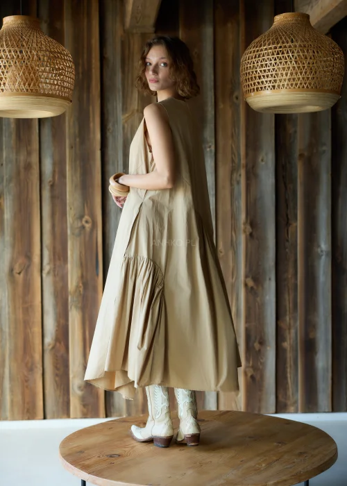 Camelowa sukienka midi o luźnym kroju bez rękawów, z asymetrycznym marszczeniem i rozcięciem, styl casual z kowbojkami.