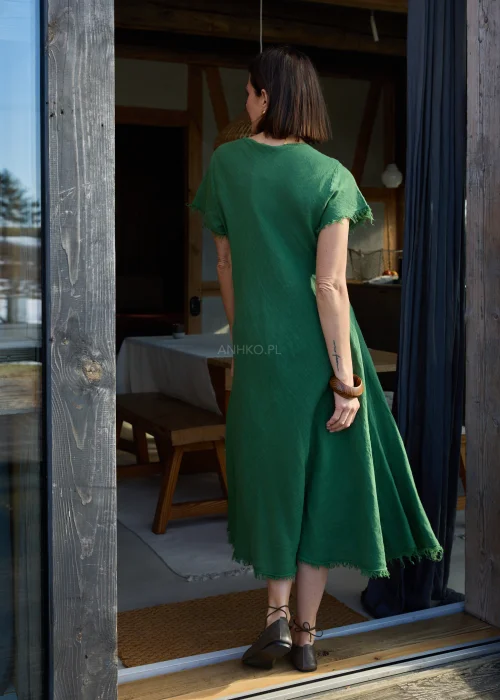 Zielona lniana sukienka midi o luźnym kroju z krótkim rękawem i surowym wykończeniem, lekko rozkloszowany fason, styl casual z balerinami.