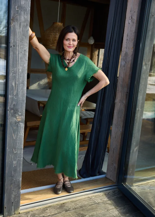 Zielona lniana sukienka midi o luźnym kroju z krótkim rękawem i surowym wykończeniem, lekko rozkloszowany fason, styl casual z balerinami.