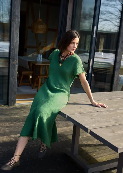 Zielona lniana sukienka midi o luźnym kroju z krótkim rękawem i surowym wykończeniem, lekko rozkloszowany fason, styl casual z balerinami.