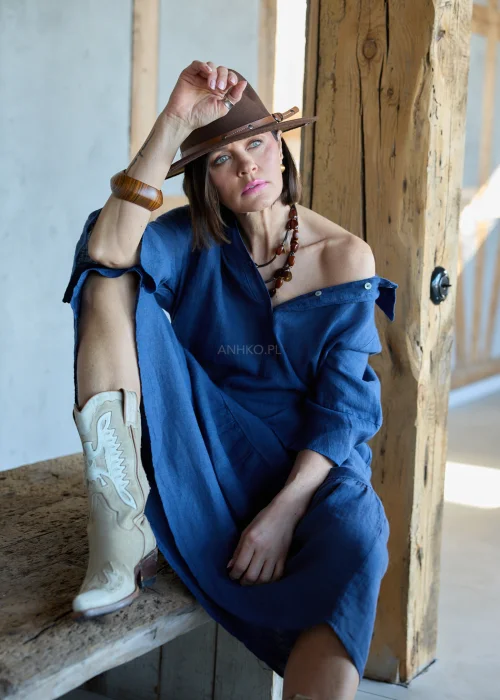 Granatowa lniana sukienka midi o luźnym kroju z kołnierzykiem i guzikami, z falbaną u dołu i rękawem 3/4, styl boho z kapeluszem i kowbojkami.