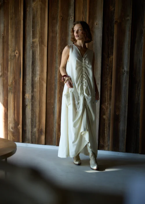 Kremowa sukienka maxi bez rękawów z szerokimi ramiączkami, marszczeniem z przodu i kieszeniami, o luźnym fasonie.