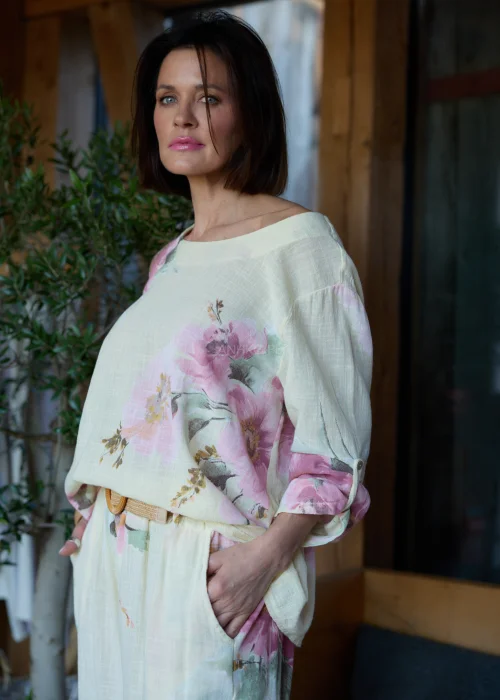 Bluzka damska w cytrynowym odcieniu z pastelowym kwiatowym printem, o luźnym kroju z rękawami 3/4 i podwijanymi mankietami, stylizowana z szerokimi spodniami w eleganckim, naturalnym zestawie.