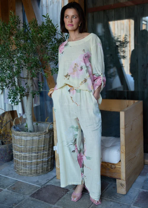 Bluzka damska w cytrynowym odcieniu z pastelowym kwiatowym printem, o luźnym kroju z rękawami 3/4 i podwijanymi mankietami, stylizowana z szerokimi spodniami w eleganckim, naturalnym zestawie.