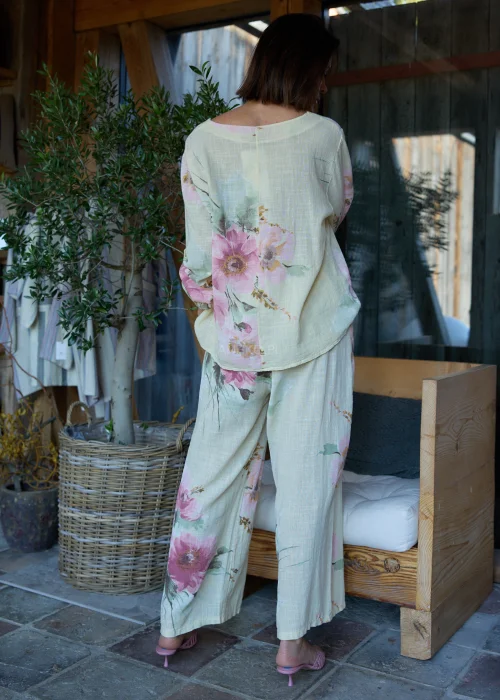 Bluzka damska w cytrynowym odcieniu z pastelowym kwiatowym printem, o luźnym kroju z rękawami 3/4 i podwijanymi mankietami, stylizowana z szerokimi spodniami w eleganckim, naturalnym zestawie.