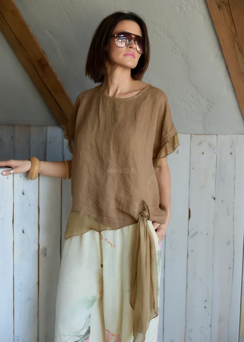 Lniana bluzka damska w jasnobrązowym kolorze z falbankami przy rękawach i wiązaniem na plecach, stylizacja z lekkimi spodniami w naturalnym stylu.