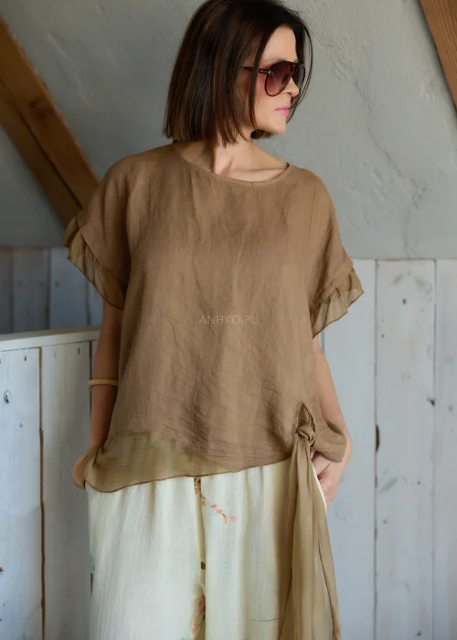 Lniana bluzka damska w jasnobrązowym kolorze z falbankami przy rękawach i wiązaniem na plecach, stylizacja z lekkimi spodniami w naturalnym stylu.