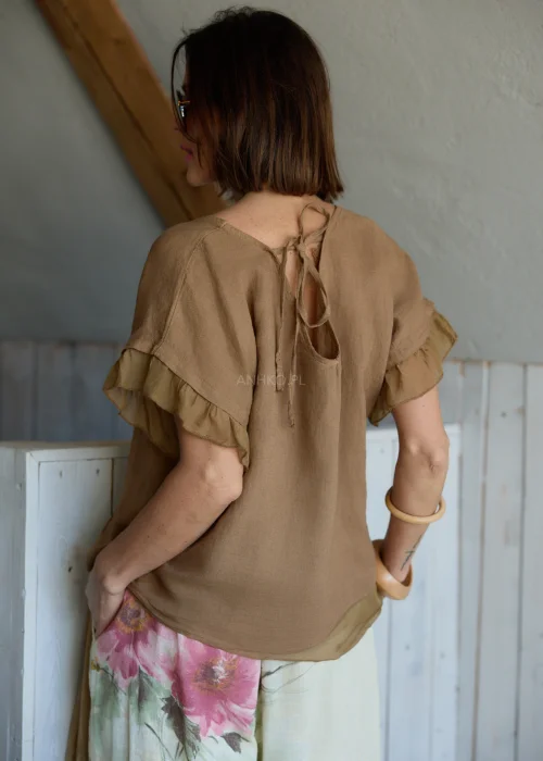 Lniana bluzka damska w jasnobrązowym kolorze z falbankami przy rękawach i wiązaniem na plecach, stylizacja z lekkimi spodniami w naturalnym stylu.