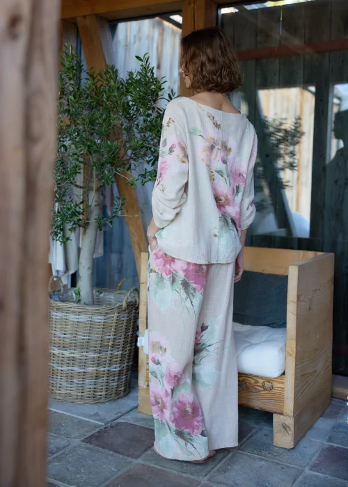 Beżowe szerokie spodnie damskie z kwiatowym printem, z wysokim stanem i paskiem w talii, o lekkim, zwiewnym fasonie, stylizowane w naturalnym, eleganckim looku.