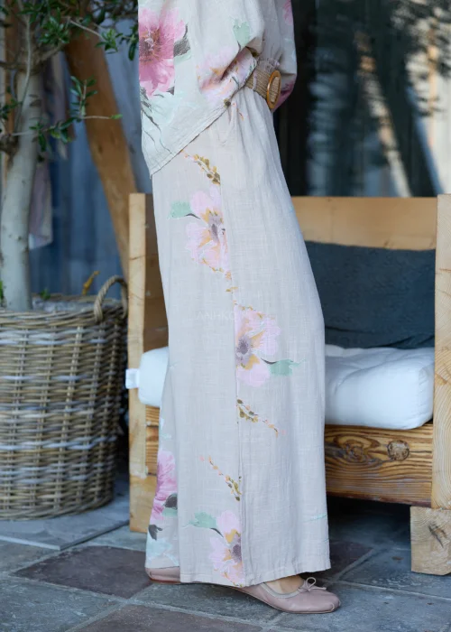 Beżowe szerokie spodnie damskie z kwiatowym printem, z wysokim stanem i paskiem w talii, o lekkim, zwiewnym fasonie, stylizowane w naturalnym, eleganckim looku.