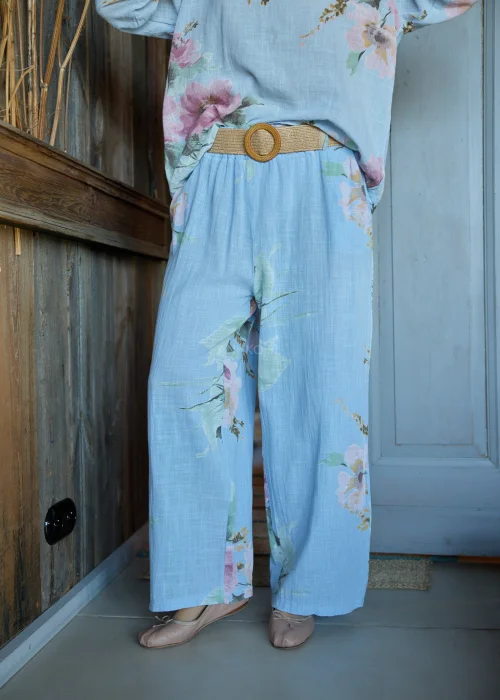 Spodnie damskie w kolorze błękitnym z kwiatowym printem, o szerokich nogawkach, stylizowane z dopasowaną bluzką i paskiem w naturalnym stylu.