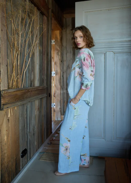 Bluzka damska w kolorze błękitnym z kwiatowym printem, o luźnym kroju, stylizowana z jasnymi spodniami i paskiem w naturalnym stylu.