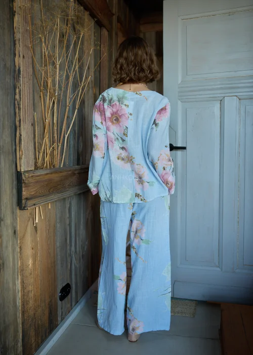 Bluzka damska w kolorze błękitnym z kwiatowym printem, o luźnym kroju, stylizowana z jasnymi spodniami i paskiem w naturalnym stylu.