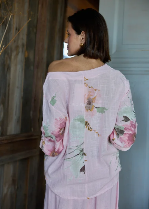 Różowa bluzka damska z kwiatowym printem, o luźnym kroju i odkrytym ramieniu, stylizowana ze spódnicą w tym samym kolorze w naturalnym, kobiecym looku.