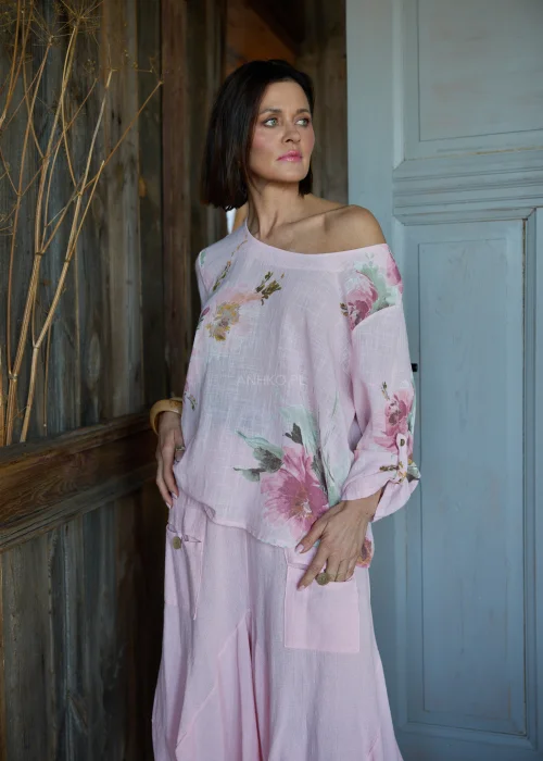 Różowa bluzka damska z kwiatowym printem, o luźnym kroju i odkrytym ramieniu, stylizowana ze spódnicą w tym samym kolorze w naturalnym, kobiecym looku.