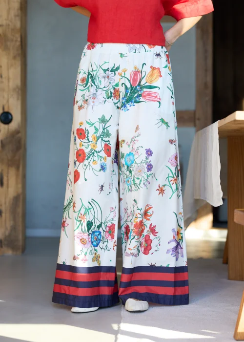 Białe spodnie damskie typu wide leg w kolorowy kwiatowy wzór z szeroką nogawką i elastycznym pasem, wykończone kontrastowym paskiem, styl casual premium.