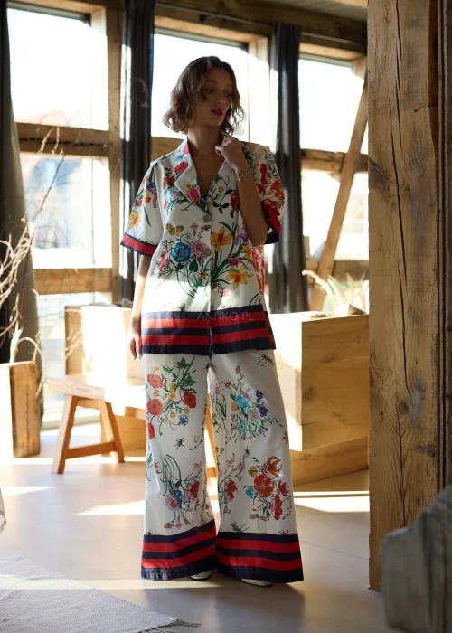 Białe spodnie damskie typu wide leg w kolorowy kwiatowy wzór z szeroką nogawką i elastycznym pasem, wykończone kontrastowym paskiem, styl casual premium.