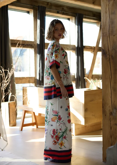 Białe spodnie damskie typu wide leg w kolorowy kwiatowy wzór z szeroką nogawką i elastycznym pasem, wykończone kontrastowym paskiem, styl casual premium.