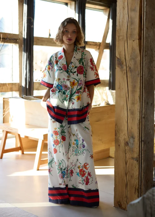 Białe spodnie damskie typu wide leg w kolorowy kwiatowy wzór z szeroką nogawką i elastycznym pasem, wykończone kontrastowym paskiem, styl casual premium.