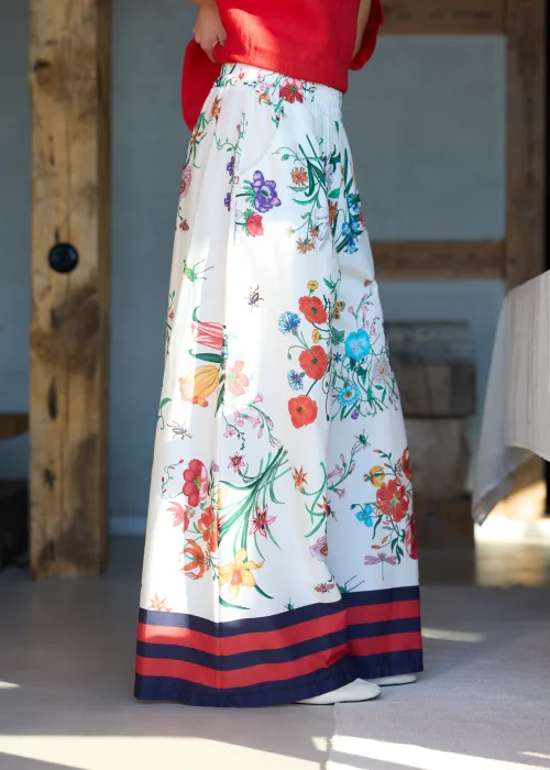 Białe spodnie damskie typu wide leg w kolorowy kwiatowy wzór z szeroką nogawką i elastycznym pasem, wykończone kontrastowym paskiem, styl casual premium.