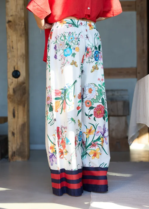 Białe spodnie damskie typu wide leg w kolorowy kwiatowy wzór z szeroką nogawką i elastycznym pasem, wykończone kontrastowym paskiem, styl casual premium.