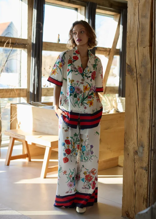 Białe spodnie damskie typu wide leg w kolorowy kwiatowy wzór z szeroką nogawką i elastycznym pasem, wykończone kontrastowym paskiem, styl casual premium.