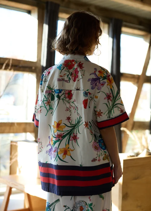 Biała koszula damska oversize w kolorowy kwiatowy wzór z krótkim rękawem i kołnierzykiem, wykończona kontrastowym paskiem.