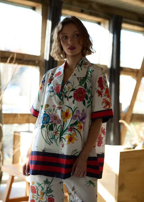 Biała koszula damska oversize w kolorowy kwiatowy wzór z krótkim rękawem i kołnierzykiem, wykończona kontrastowym paskiem.