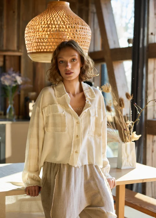 Lniana koszula damska w kolorze kremowym, o luźnym kroju, zapinana na guziki, z naszywanymi kieszeniami i surowym wykończeniem.