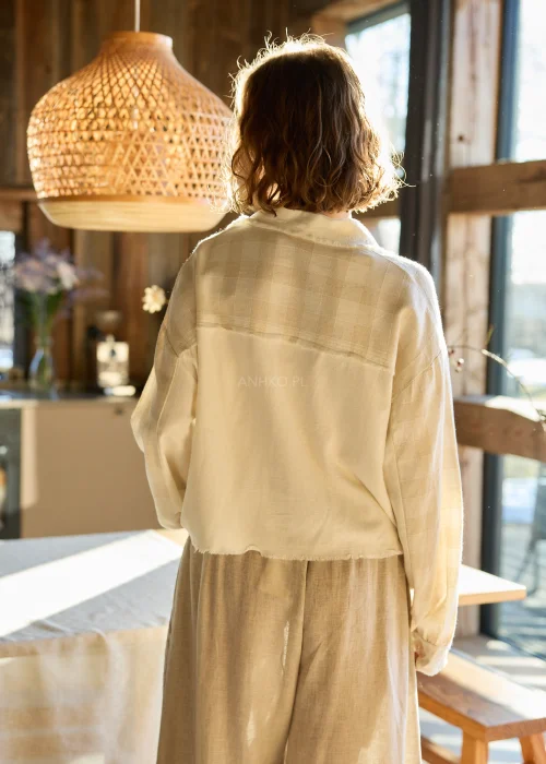 Lniana koszula damska w kolorze kremowym, o luźnym kroju, zapinana na guziki, z naszywanymi kieszeniami i surowym wykończeniem.