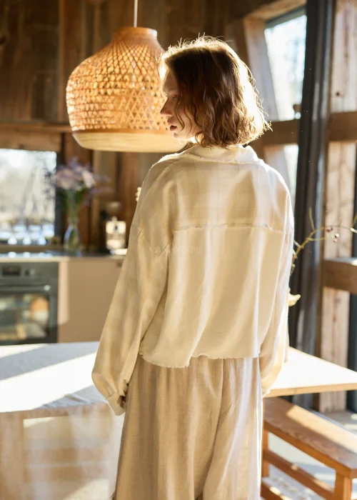 Lniana koszula damska w kolorze kremowym, o luźnym kroju, zapinana na guziki, z naszywanymi kieszeniami i surowym wykończeniem.