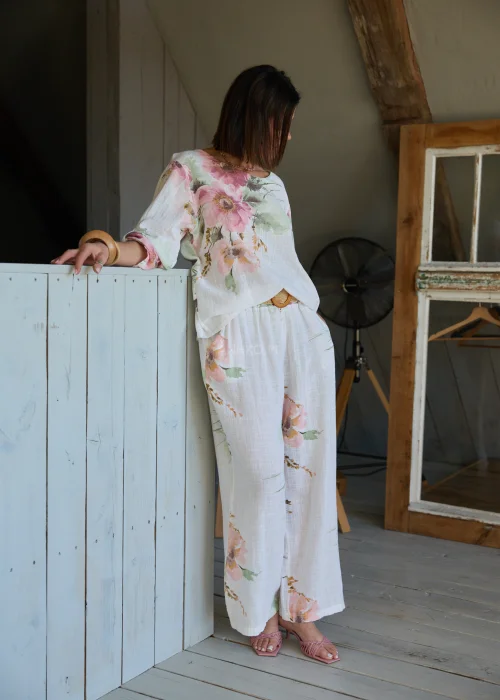 Bluzka damska w kolorze białym z delikatnym kwiatowym printem, luźny fason z podwijanymi rękawami, stylizowana z szerokimi spodniami i paskiem w naturalnym, eleganckim looku.