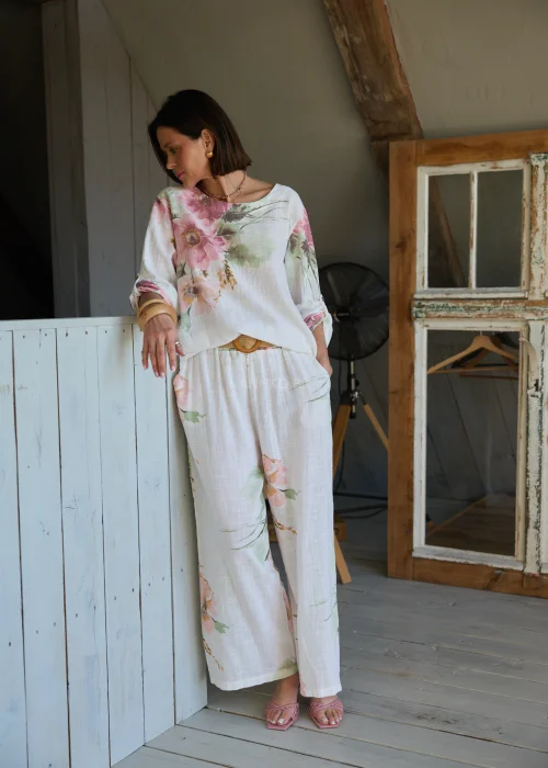 Bluzka damska w kolorze białym z delikatnym kwiatowym printem, luźny fason z podwijanymi rękawami, stylizowana z szerokimi spodniami i paskiem w naturalnym, eleganckim looku.