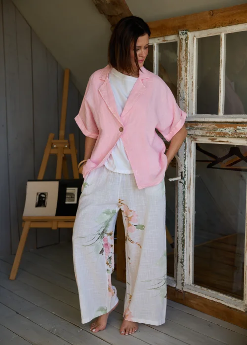 Lniana marynarka damska w kolorze różowym, luźny fason z krótkim rękawem i lekką strukturą tkaniny, stylizowana warstwowo z topem i spodniami w kwiatowy print.
