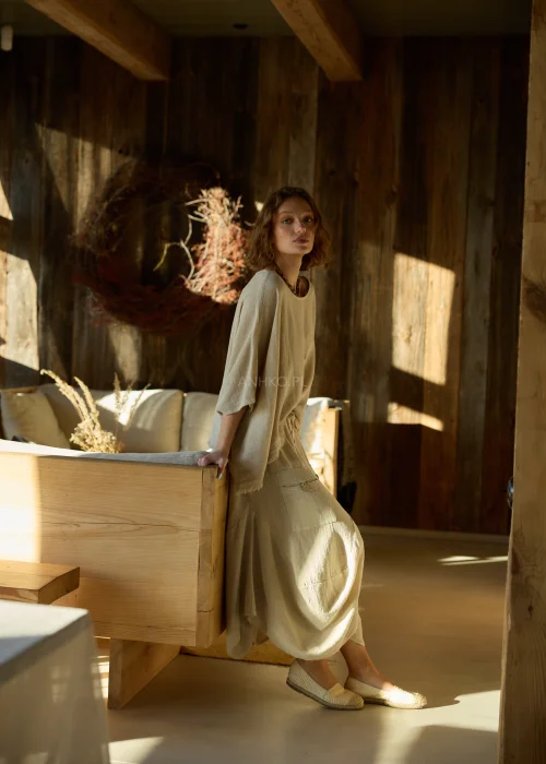 Beżowa bluzka damska oversize z dodatkiem lnu, o luźnym kroju i szerokich rękawach, stylizowana z naturalnymi dodatkami w ciepłym wnętrzu.