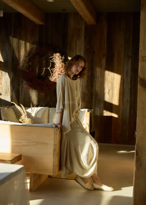 Beżowa bluzka damska oversize z dodatkiem lnu, o luźnym kroju i szerokich rękawach, stylizowana z naturalnymi dodatkami w ciepłym wnętrzu.