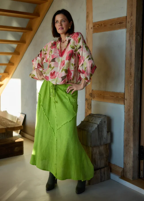 Zielona spódnica midi o luźnym kroju z surowymi przeszyciami i elastycznym pasem, stylizowana z kwiatową koszulą i botkami na obcasie w nowoczesnym looku.