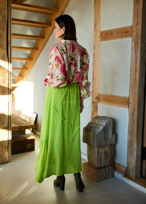 Koszula damska w kwiatowy print w odcieniach różu i zieleni, o luźnym kroju z długim rękawem, stylizowana z zieloną spódnicą midi.