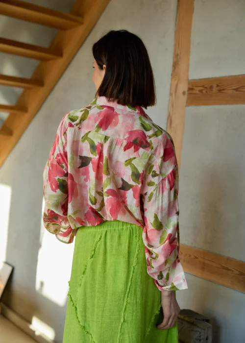 Koszula damska w kwiatowy print w odcieniach różu i zieleni, o luźnym kroju z długim rękawem, stylizowana z zieloną spódnicą midi.