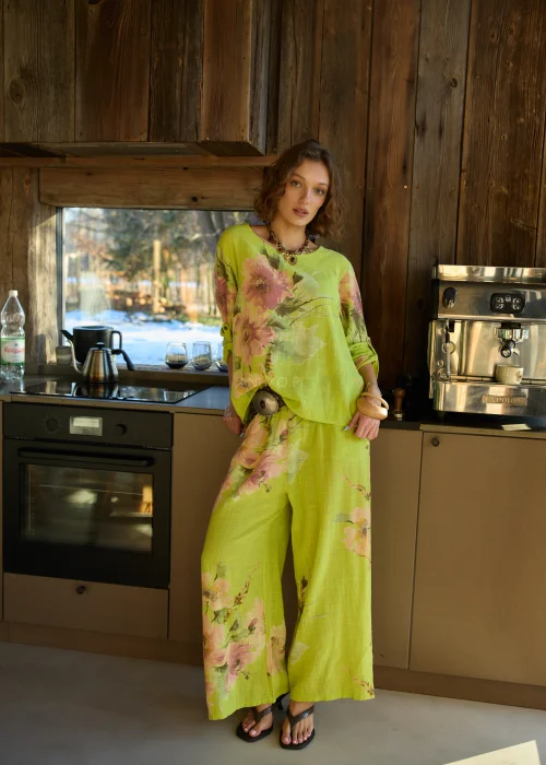 Zielone szerokie spodnie damskie z kwiatowym printem, z wysokim stanem i elastycznym pasem, stylizowane z paskiem i sandałami na obcasie w letnim, świeżym looku.