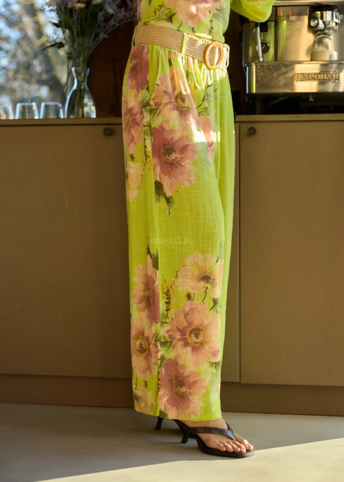 Zielone szerokie spodnie damskie z kwiatowym printem, z wysokim stanem i elastycznym pasem, stylizowane z paskiem i sandałami na obcasie w letnim, świeżym looku.