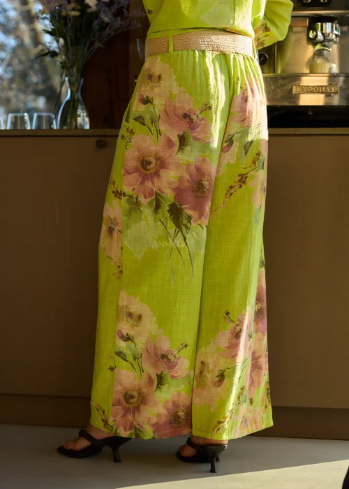 Zielone szerokie spodnie damskie z kwiatowym printem, z wysokim stanem i elastycznym pasem, stylizowane z paskiem i sandałami na obcasie w letnim, świeżym looku.